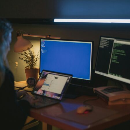 Woman using multiple screens for cybersecurity tasks in a cozy home office