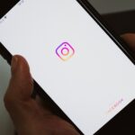 Crop faceless person taking mobile phone and demonstrating blank screen with social media app logo while having break and surfing internet