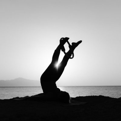 Black and white silhouette of a woman doing yoga by the ocean at sunset, emphasizing relaxation.